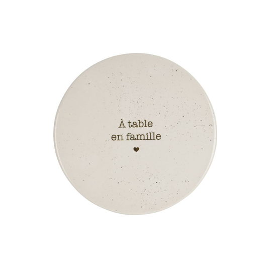 Dessous de plat rond en grès blanc moucheté avec l'inscription À table en famille et un petit cœur, marque SEMA Design.