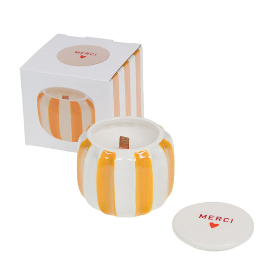 Bougie parfumée dans un pot en céramique à rayures orange et blanc avec son couvercle marqué Merci et son emballage cadeau.