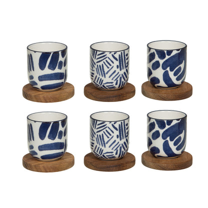 Assortiment de 6 tasses espresso en grès blanc et bleu avec motifs géométriques et leurs sous-tasses rondes en bois naturel.